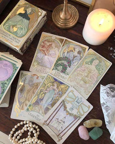 some cards are sitting on a table next to a candle and pearls, with a beaded bracelet around them