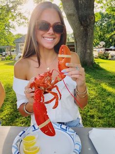 a woman holding up a lobster on a plate with lemons and water in front of her