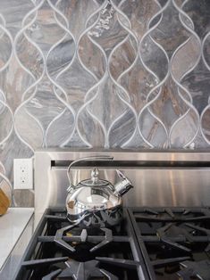 a tea kettle sitting on top of a stove next to a wallpapered backsplash