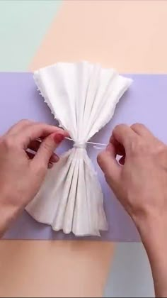 two hands are holding a piece of white tissue paper and stringing it with scissors