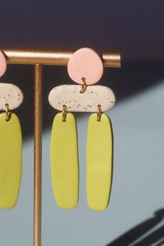 two pairs of yellow and pink earrings hanging from a gold hook on a metal pole