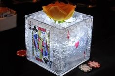 an ice cube with playing cards and a yellow rose in it on a black table