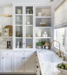 a kitchen with white cabinets and marble counter tops, gold faucets and green apples