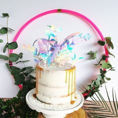 a white cake with frosting and flowers on top sitting in front of greenery