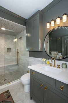 a bathroom with gray cabinets and a white toilet next to a walk - in shower