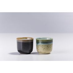 two cups sitting next to each other on a white tableclothed surface, one with black and green glaze