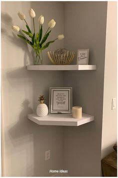 two white shelves with flowers and pictures on them in a room that is painted gray