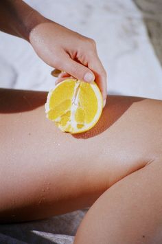 a person holding an orange slice in their left hand while laying on the sand at the beach