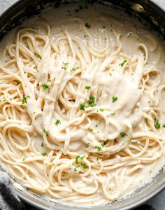 a pan filled with pasta covered in white sauce and parsley sprinkled on top