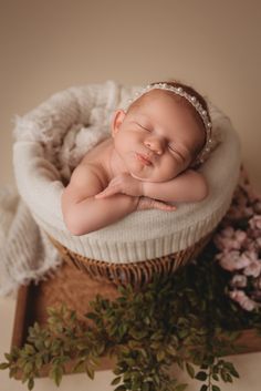 a newborn baby sleeping in a basket with flowers on the side and greenery around it