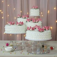 three tiered white wedding cake with pink flowers on top and cupcakes in the middle