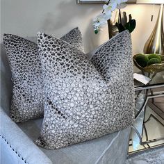 two decorative pillows sitting on top of a couch next to a vase with flowers in it