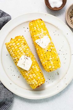 two corn on the cob with butter and seasoning sitting on a white plate