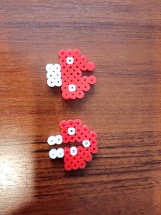 two pieces of red and white perler bead on a wooden table with one piece missing