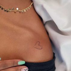 a woman's stomach with a small heart tattoo on her left side ribcage