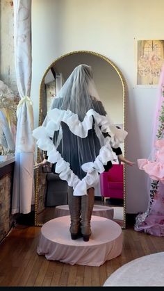 a woman is standing in front of a mirror wearing a veil and boots with ruffles on it