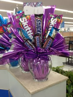 a purple vase filled with candy bars and wrapped in purple ribbon sitting on top of a counter