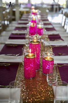 the table is set with pink candles and purple napkins on it, along with gold sequin - covered place mats