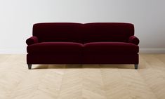 a red couch sitting on top of a hard wood floor next to a white wall