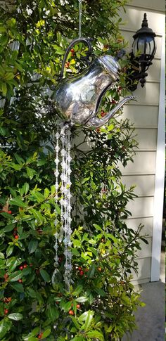 a metal teapot hanging from a tree in front of a house