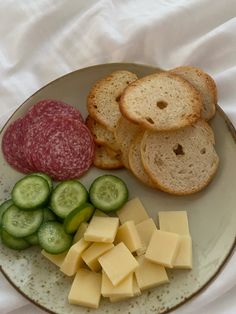 a plate with bread, cucumbers, cheese and meat on it next to slices of bread