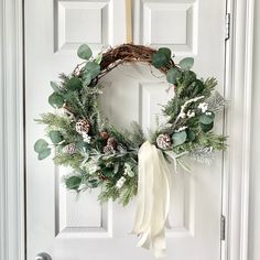 a wreath with pine cones, evergreen leaves and white berries hangs on the front door