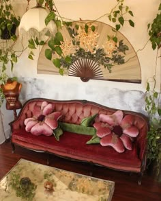 a red couch with pink flowers on it in front of a fan and other decorations