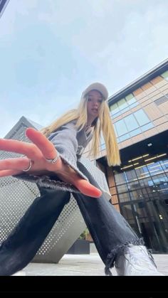 a woman sitting on top of a skateboard in front of a building with her hand out