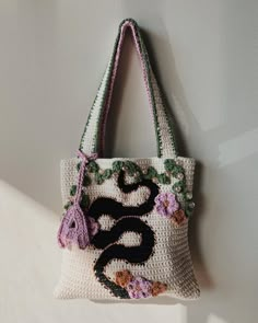 a crocheted bag hanging on the wall with flowers and leaves around it's handles