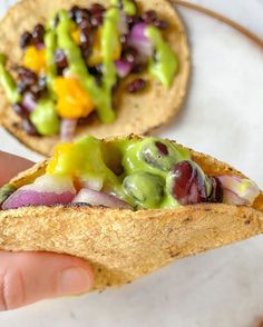 a hand is holding a tortilla filled with vegetables and other toppings on it