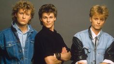 three young men standing next to each other in front of a gray background with their arms crossed