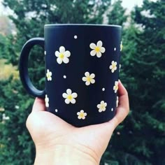 a hand holding a black coffee mug with white and yellow flowers on it