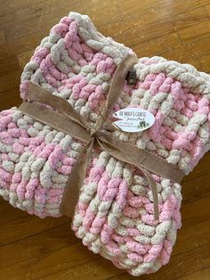 three pink and white crocheted blankets wrapped in brown ribbon on top of a wooden floor