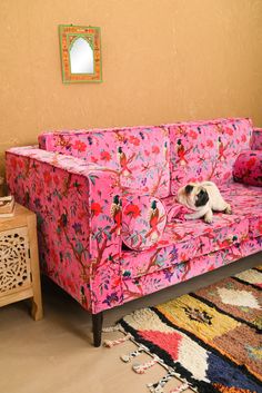 a dog laying on top of a pink couch in a living room next to a rug