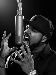 a man singing into a microphone in front of a black and white photo with his hands up