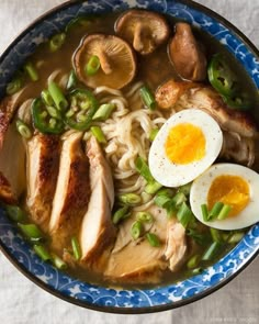 a blue bowl filled with noodles, meat and mushrooms next to an egg on top