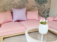 a pink couch sitting next to a white table with flowers in a vase on it