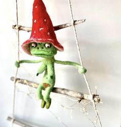 a stuffed frog with a red hat hanging from a branch