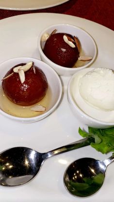 three desserts in small bowls on a white plate with spoons next to them