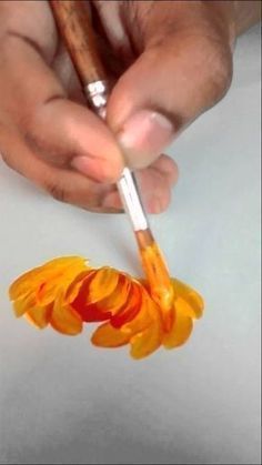 a person holding a paintbrush in their left hand and painting the petals on paper