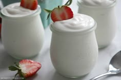 three glasses filled with yogurt and two strawberries on the table next to each other