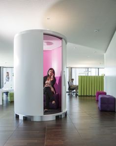 a woman sitting on a purple chair in a room with pink and green walls, while talking on her cell phone