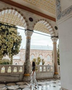 a woman in white is walking through an ornately decorated building with arches and columns