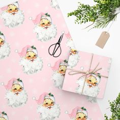 pink wrapping paper with santa claus on it next to green plants and scissors for cutting