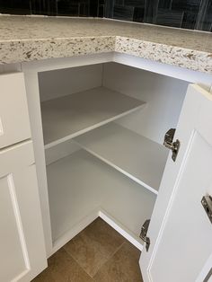 an open cabinet in a kitchen with marble counter tops