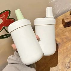 a person holding two baby bottles in their hands, one white and the other green