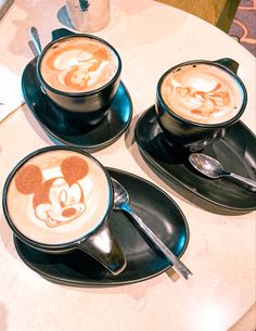 three cups of coffee with mickey mouse designs on them and spoons next to each other