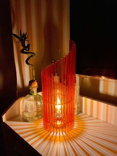 an orange glass vase sitting on top of a table next to a bottle and candle