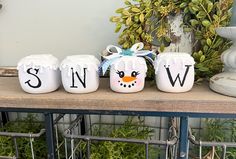 three white ceramic containers with the word snow painted on them, sitting on a shelf