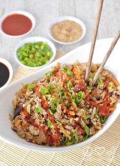 a white bowl filled with rice and veggies next to dipping sauces on a bamboo mat